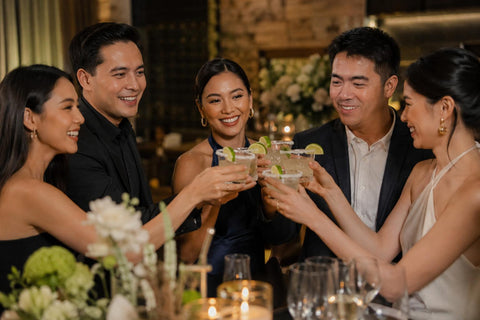 Well-dressed guests raising tequila cocktails during an elegant private celebration with warm lighting and a festive atmosphere