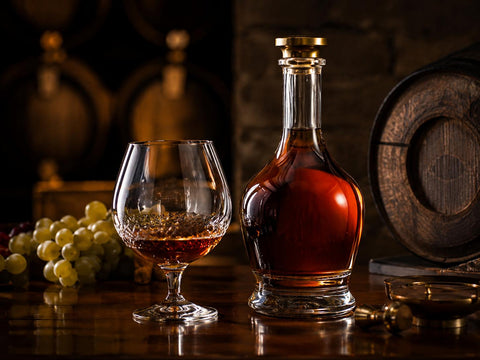 Elegant glass and unlabeled bottle of Cognac with grapes and oak barrel details in a warm premium cellar setting