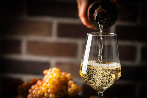 White wine being poured into a glass beside grapes, highlighting National White Wine Day and wine exploration