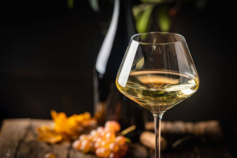 White wine glass with a bottle and grapes on a wooden table, highlighting National White Day wine selections